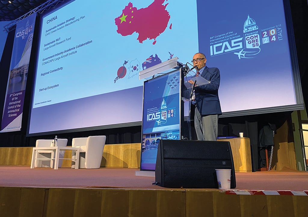 Guy Norris speaking in front of wide screen at 34th Congress of the International Council of the Aeronautical Sciences